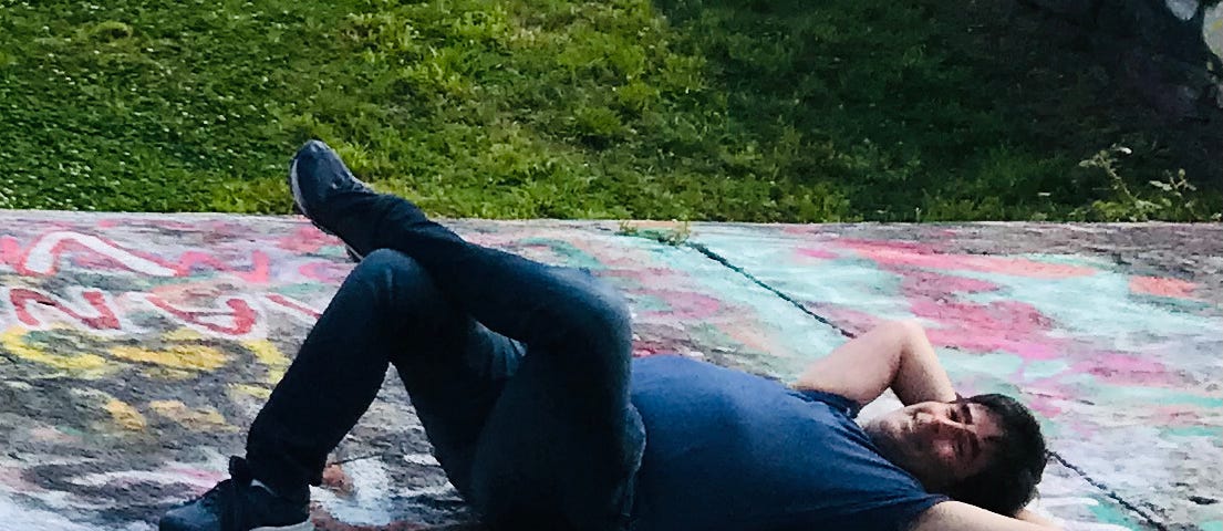 Author lying on pavement covered with colored graffiti with legs crossed and arms behind head like a pillow