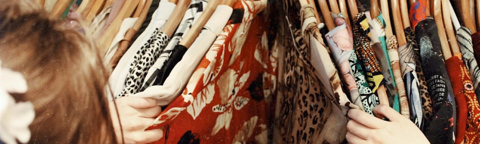 A woman selects clothes from a rack of dresses with flowers printed on them