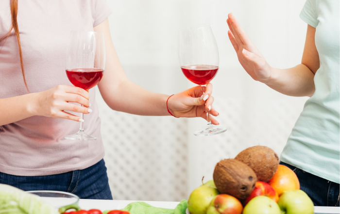 Woman refusing a glass of wine while hanging out with her friends