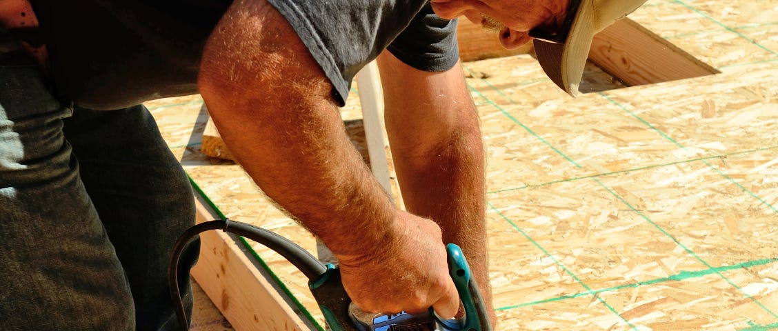 Stock photo of a contractor doing work on a house using lumber and a power tool.