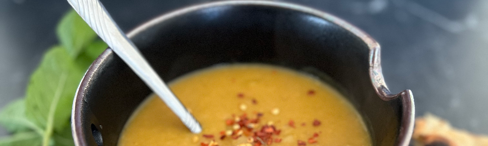 Lentil soup on a marble countertop with toasted naan and mint