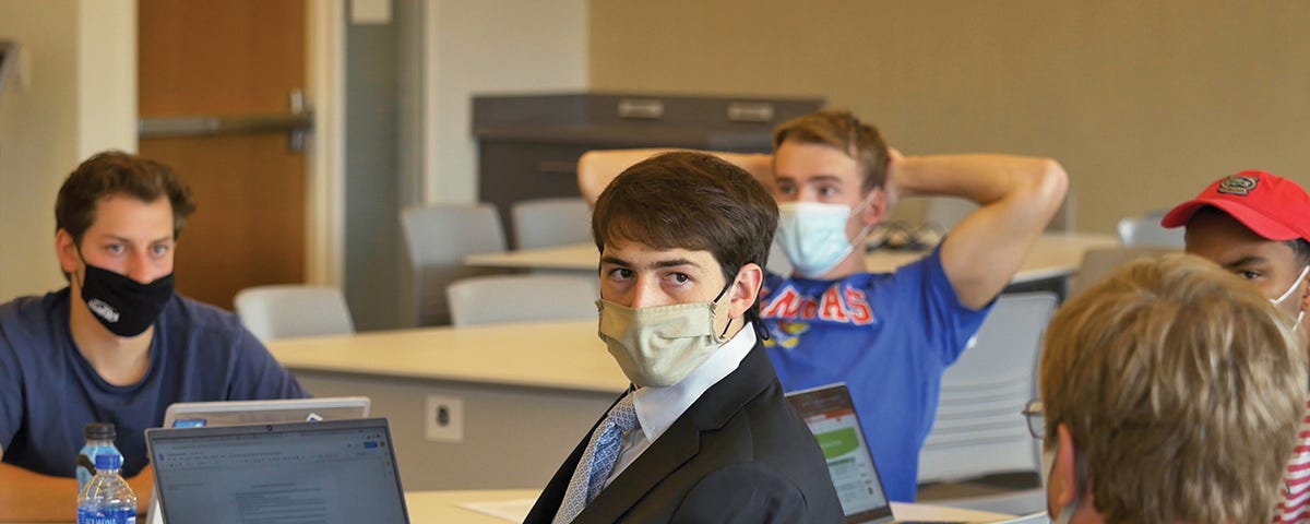 Students wearing masks and seated at desks speak with associate professor Felix Meschke