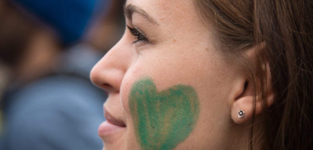 Woman with green heart painted on her cheek to show her love for nature.