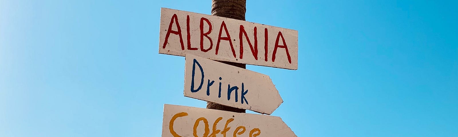 A hand written welcome sign on a beach pole in Albania showing where to get food and drinks.
