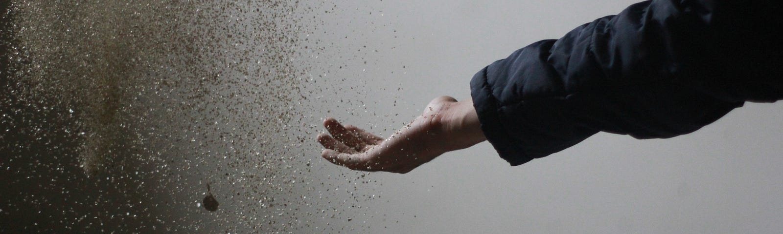 A person letting go of grains of sand.