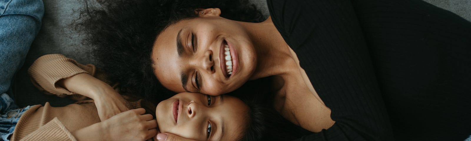 Mother and daughter of color happily laying on a bed.
