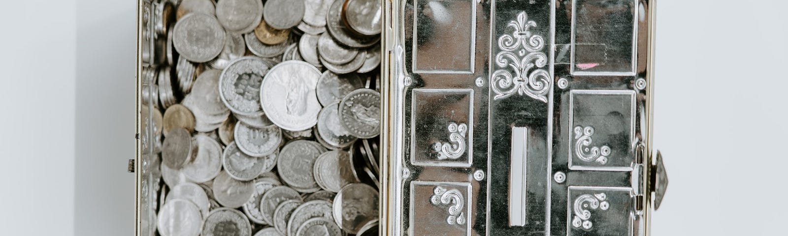 An open metal box with lots of coins inside.