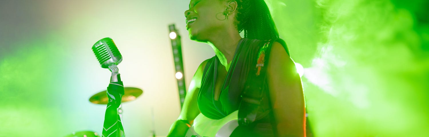 Photo of a woman singing and playing guitar, with a burst of light green color