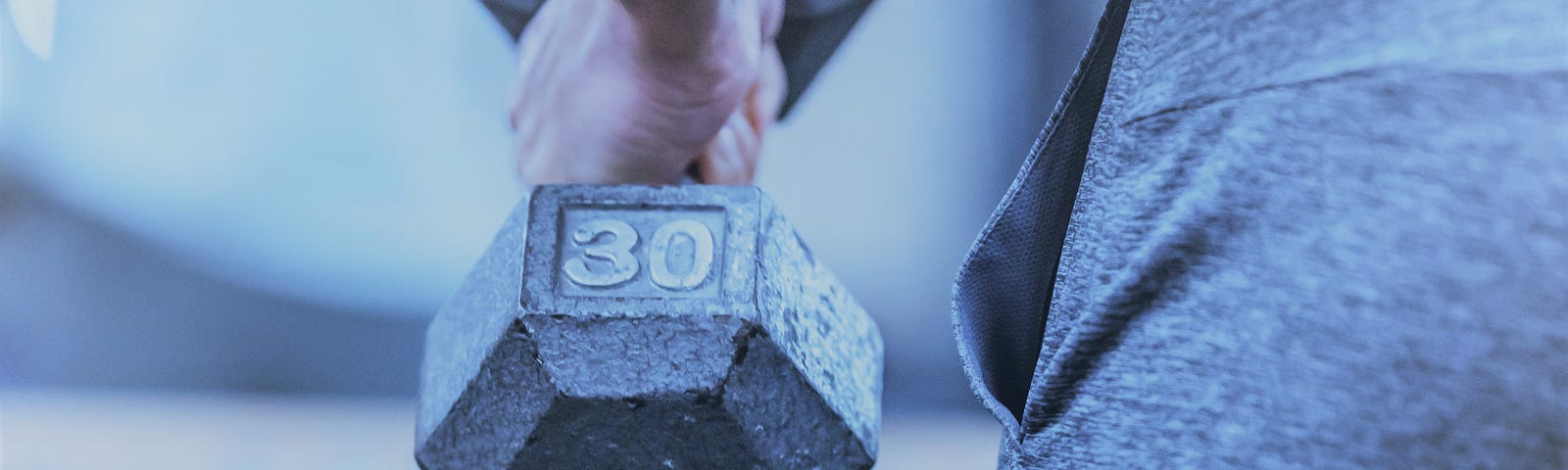 a male holding a dumbbell by his side in a gym