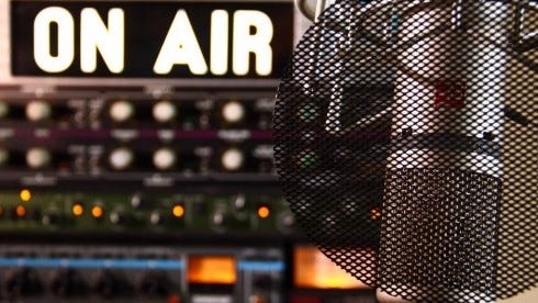 A photograph of an on-air sign that is lit up with a broadcast microphone in the corner