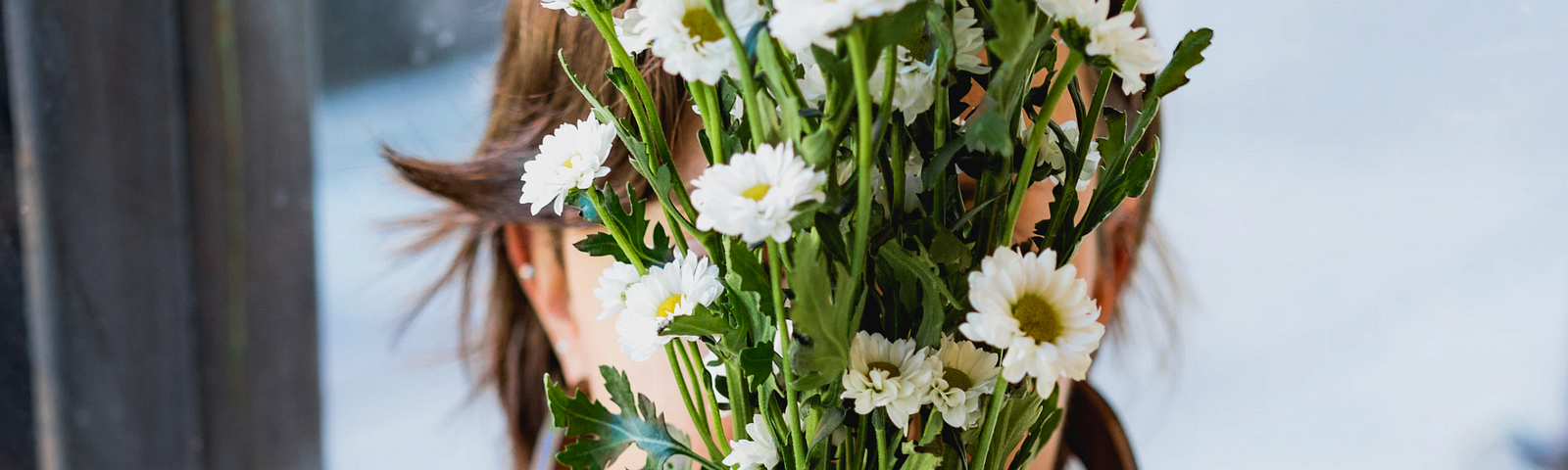 A woman holds up a bouquet of daisies in front of her face.