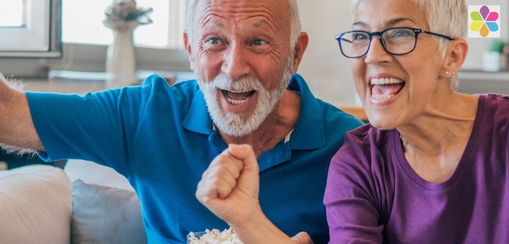 attractive older woman and man watching tv and cheering with bowl of popcorn