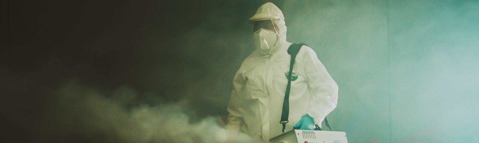 A person in a white hazmat suit uses a strange box to steam up a room.