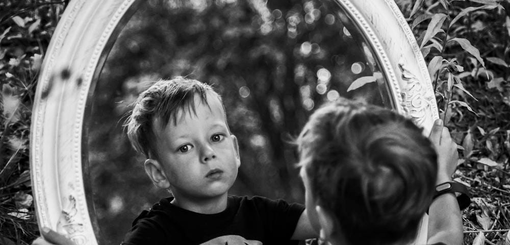 Boy looks at reflection wearing Batman symbols.