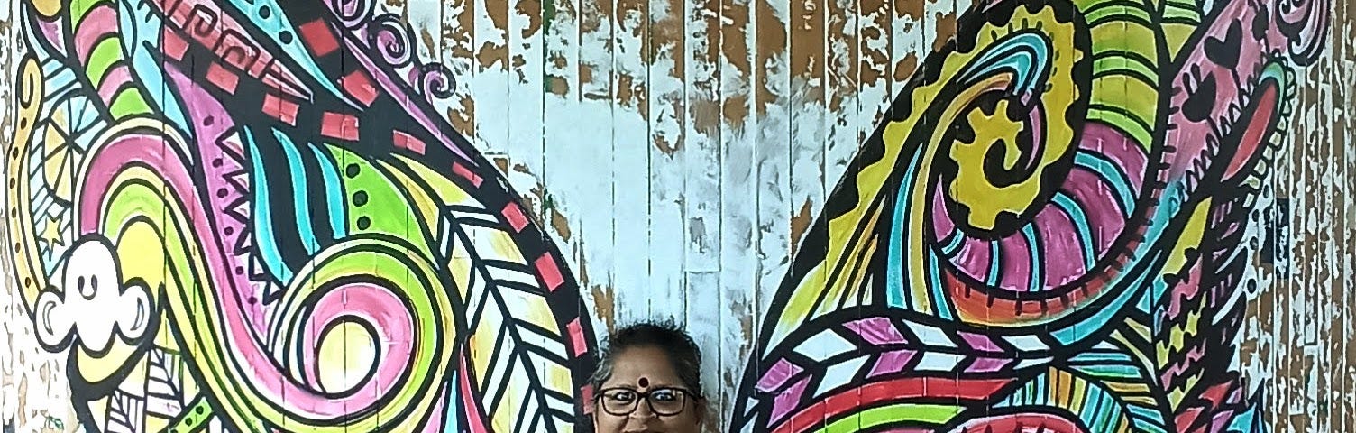 Vidya Sury standing against a wall painted with butterfly wings