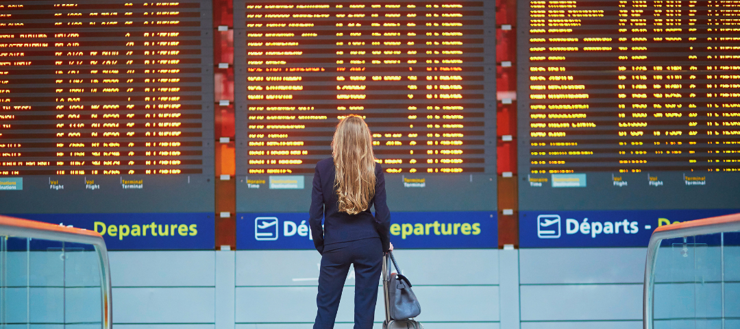 A woman with a suitcase looking at the departures board at an airport