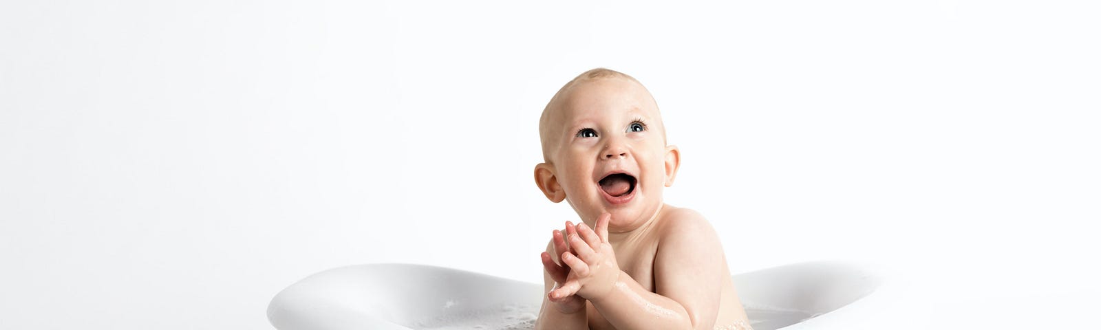 Baby sitting in a white bathtub, clapping its hands