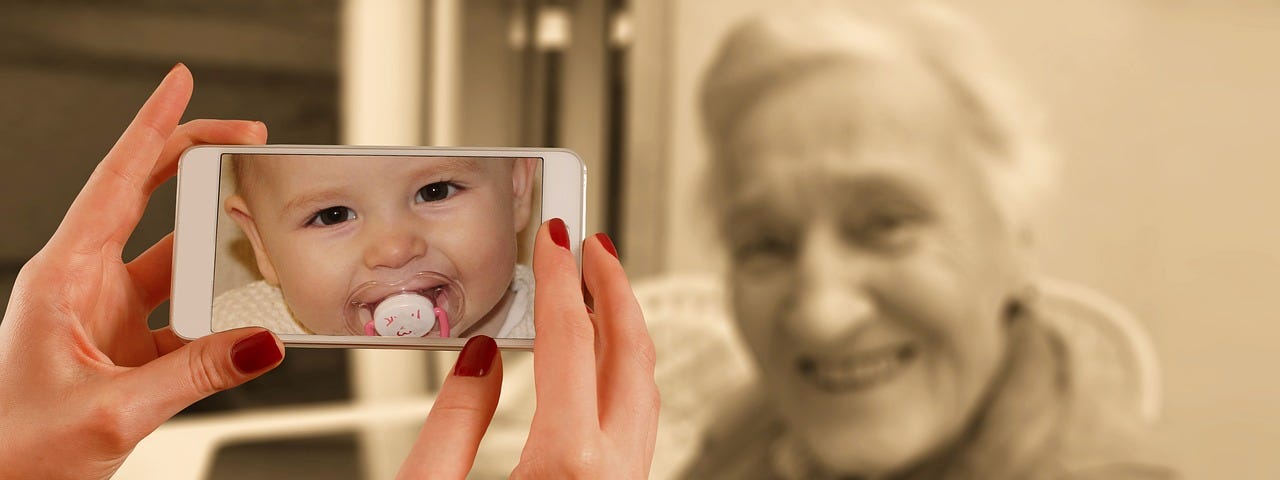 An iPhone taking a photo of an old woman, except the picture on the phone shows the woman as the beababy girl she once was.