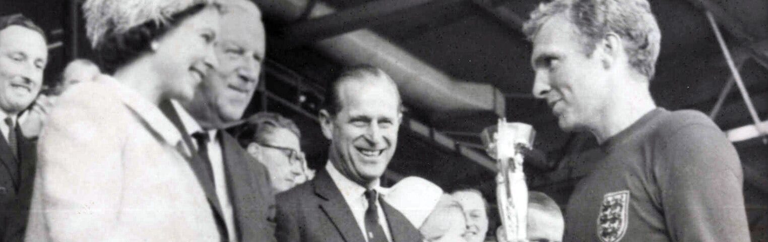 This is a black and white photograph of Queen Elizabeth II presenting the 1966 World Cup to England Captain, Bobby Moore.