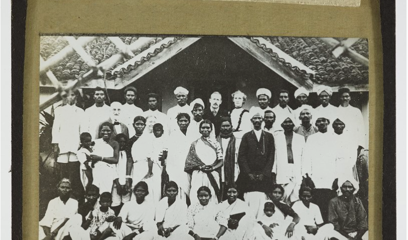 Black and white photograph of a white missionary couple (centre) surrounded by Indian men and women and children wearing white.
