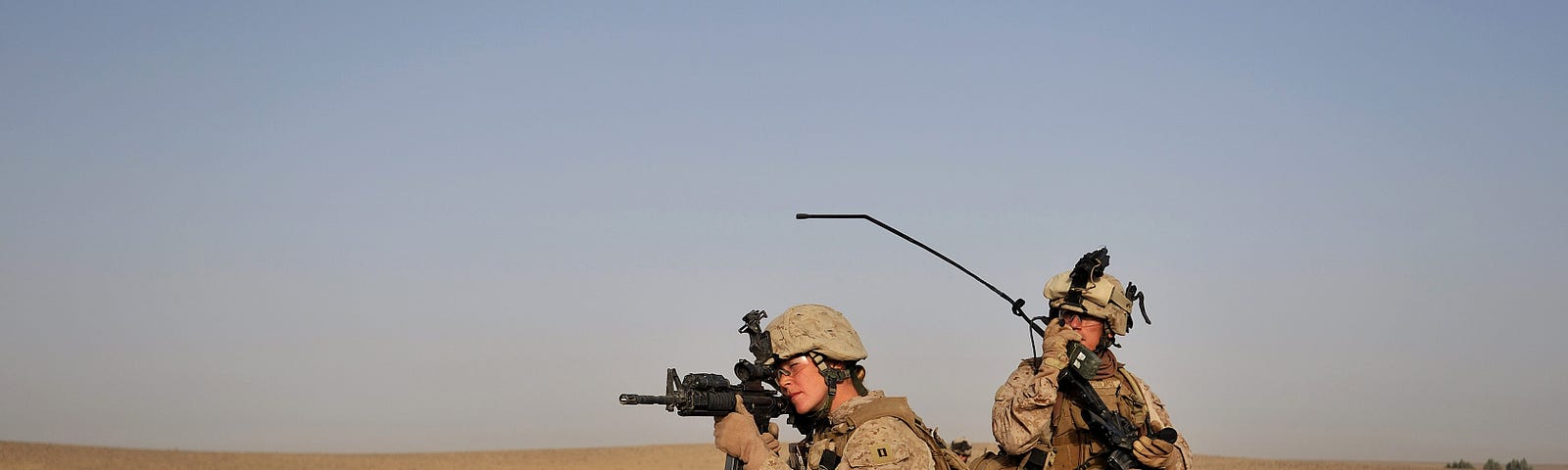 One American soldier looks down her rifile while another holds up a radio in desert near Sistani Village Afghanistan.