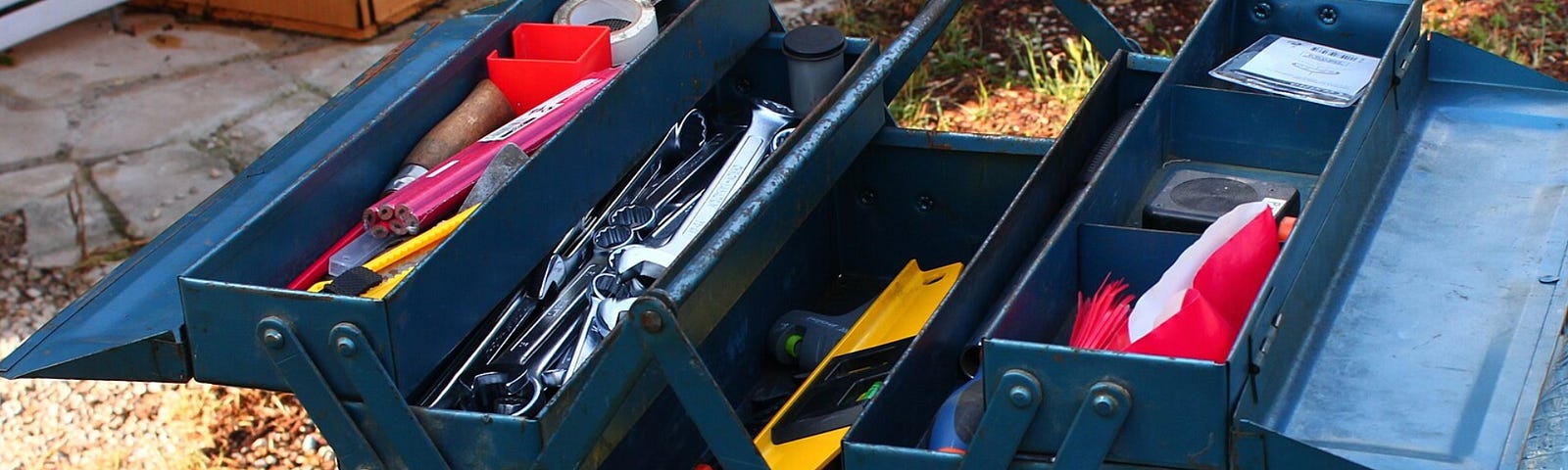 A dark blue metal tool box sits open on a gray tabletop. The tool box has five different levels of drawers to hold an array of brightly colored tools.