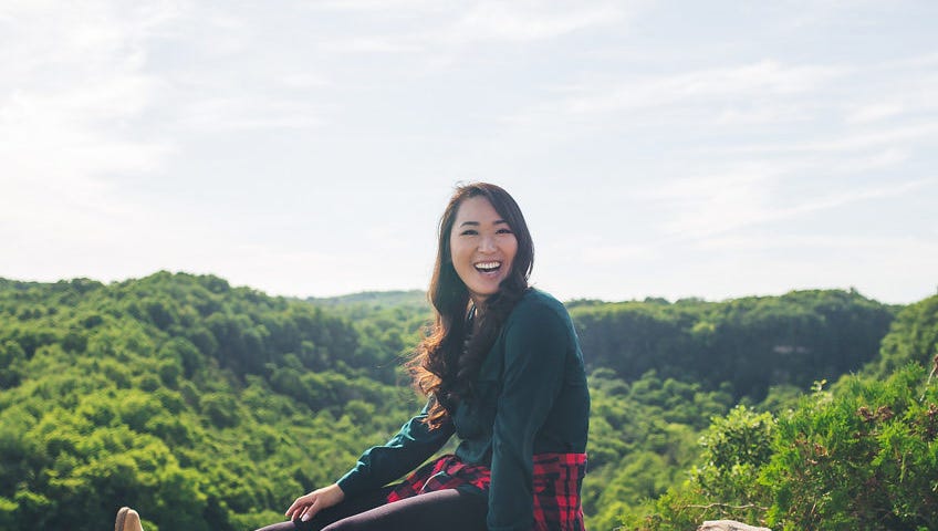 Lisa Le sits on a rocky bluff overlooking a lush forest.