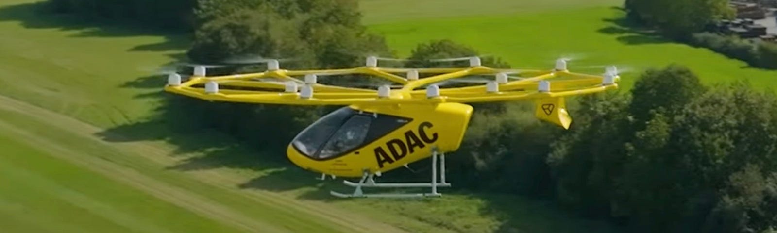 A yellow prototype Volocity air taxi taking flight from the company Volocopter over a green field