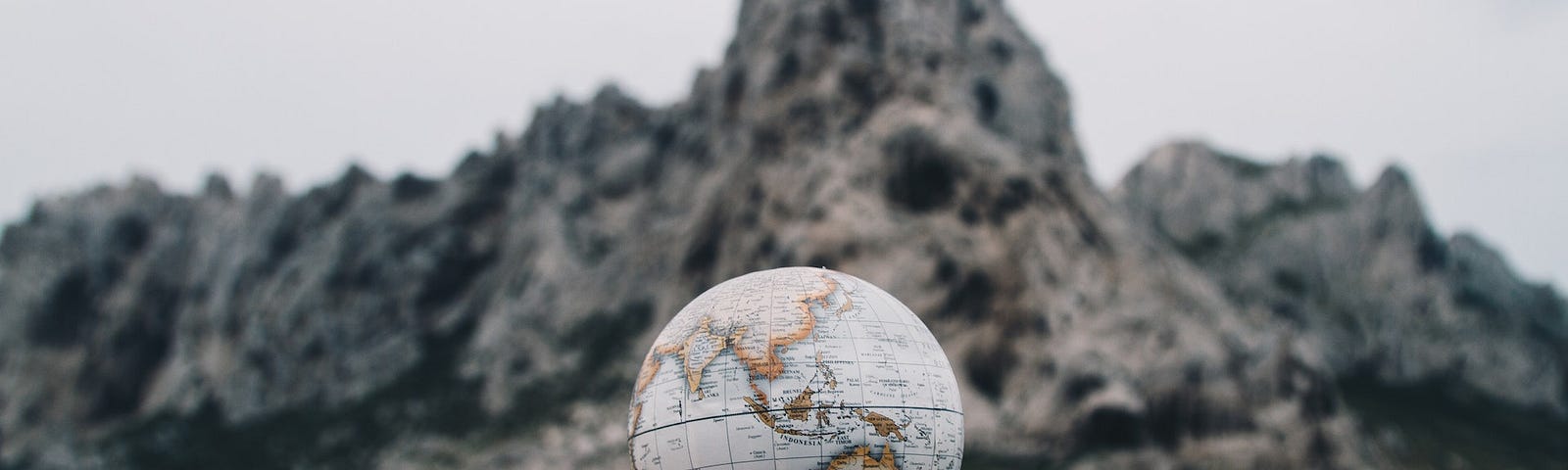 A person seemingly levitating a small Earth globe over his hand. A rocky beach is in the background.