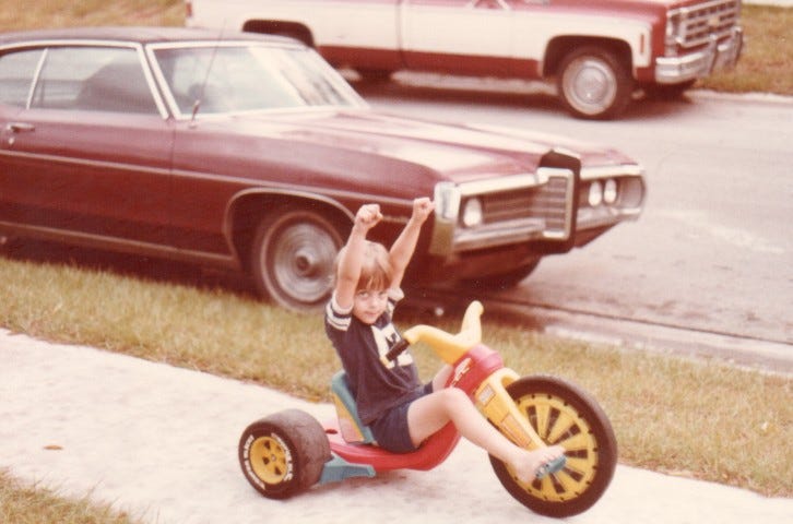 Author as a child riding a big wheel on a neighborhood sidewalk, circa 1980s.