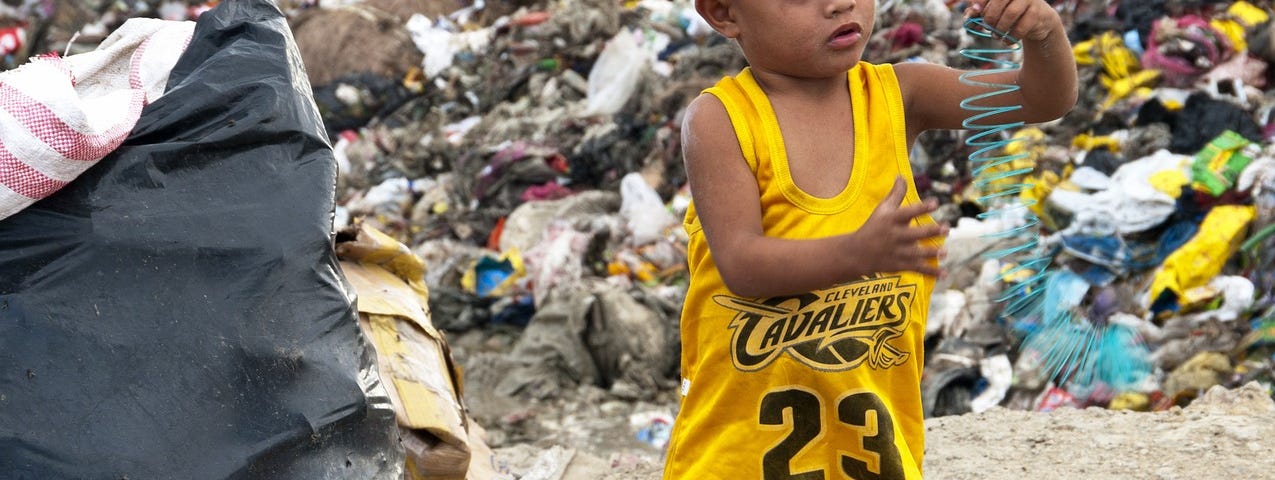 a little boy amid piles of plastic garbage in a landfill. He is playing with a plastic spring. Forever Chemicals: PFAS Plastic