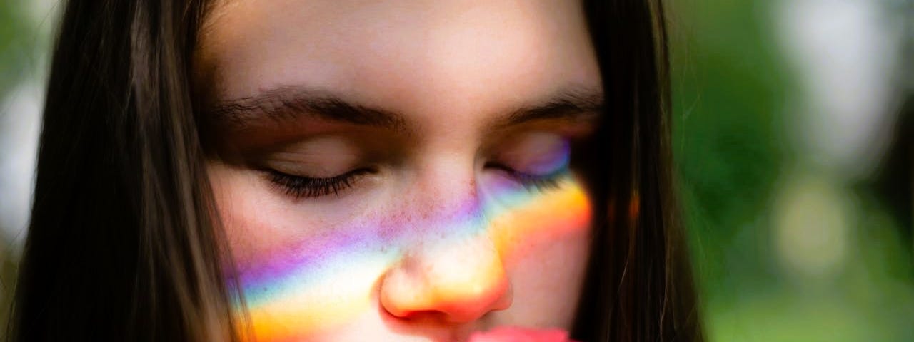 Woman smelling a rose with the reflection of a rainbow across her face