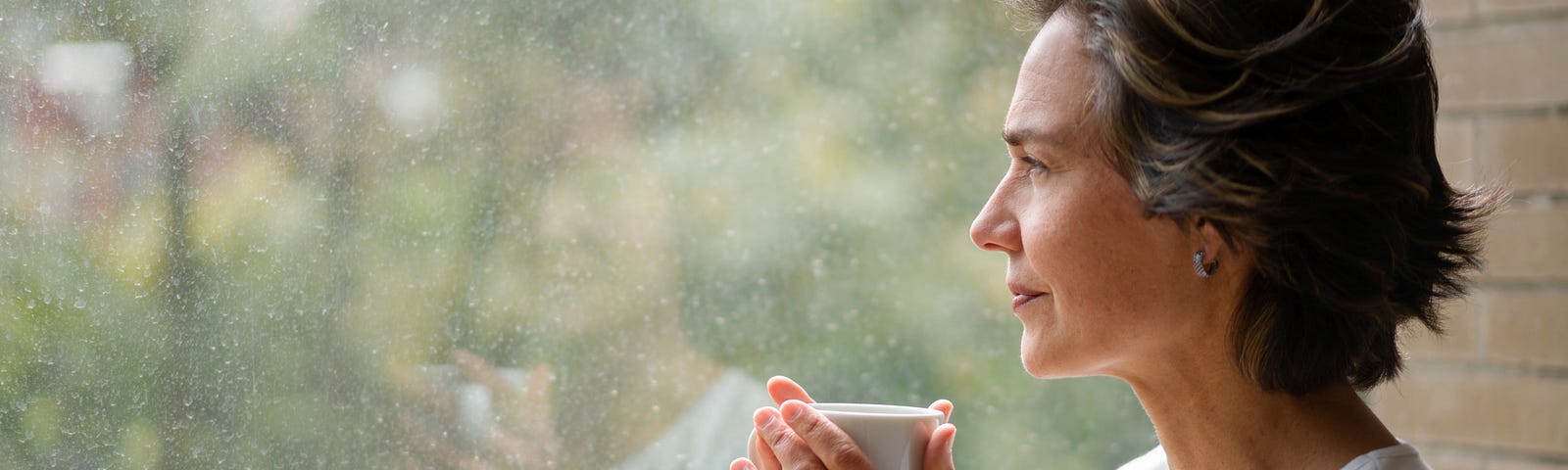 Pensive woman drinking from cup looking out a window