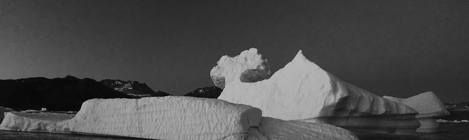 A black and white photograph of an iceberg drifting in a fjord in Greenland