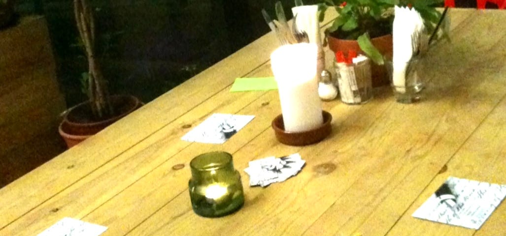 Table (light-coloured wood) with candles and plants. Create & Write Workshop cards set out pre-session.