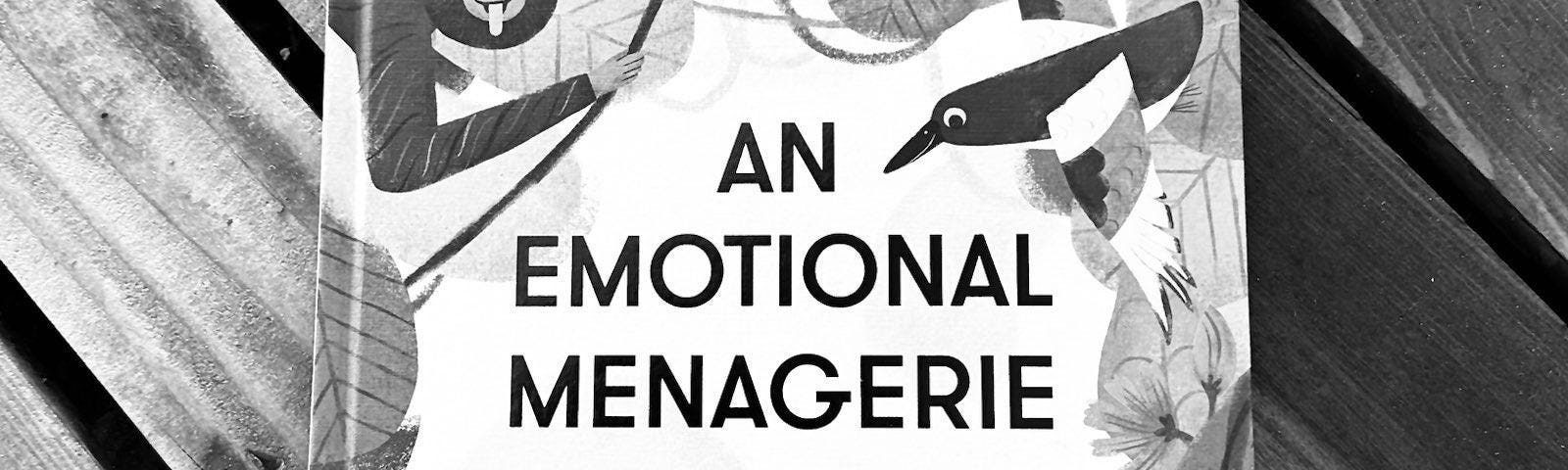 A black and white photo of the book “An emotional menagerie” over a wooden surface.