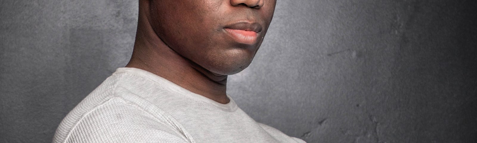 A man standing with his arms crossed in front of a grey background