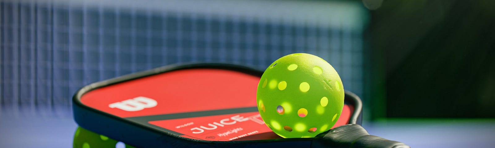 A pickleball racket sitting on three balls, with a fourth ball balanced on top