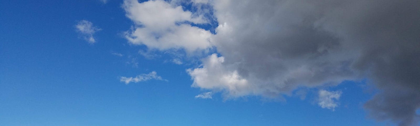 White clouds in a blue sky. In the bottom of the frame green hills and some far-away buildings sit small in the image.