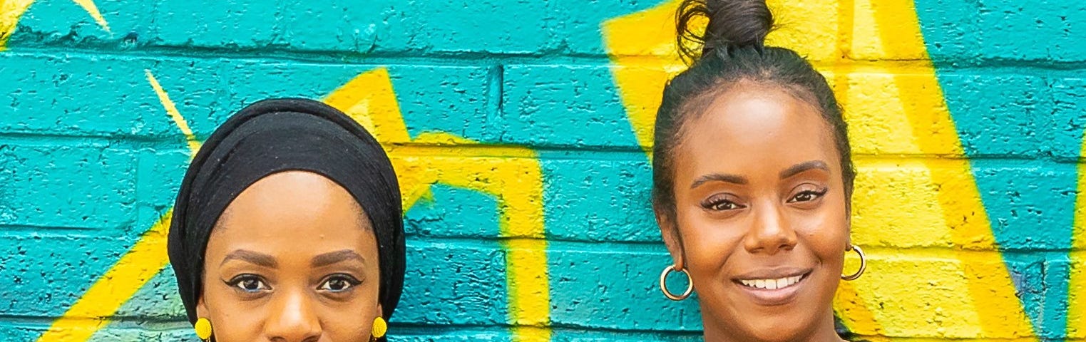Portrait of Sadiqah and Devina of Black in Data, stood together against a colourful graffittied wall