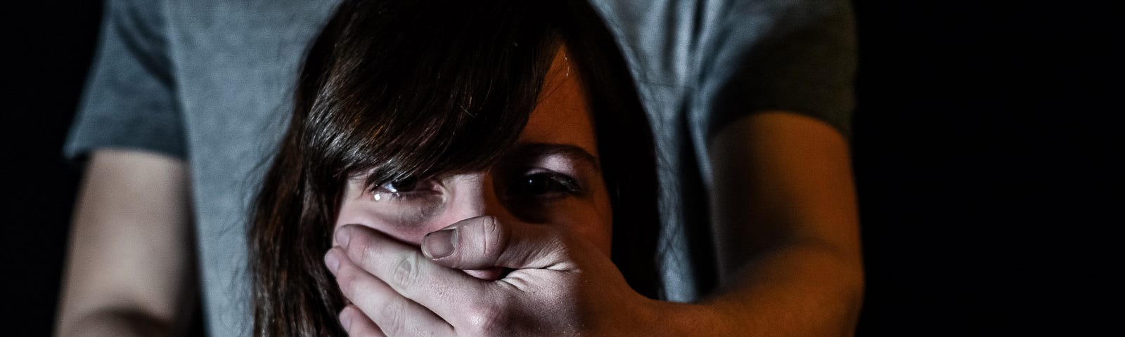 A woman cries silently as her partner covers her mouth forcefully with his hand from behind.