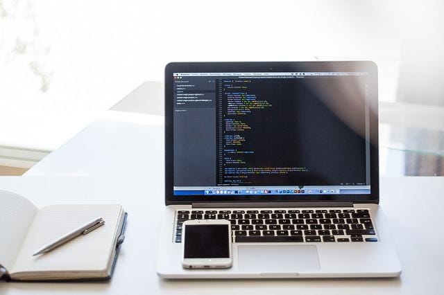 Photo of a laptop, phone, and notebook with a pen