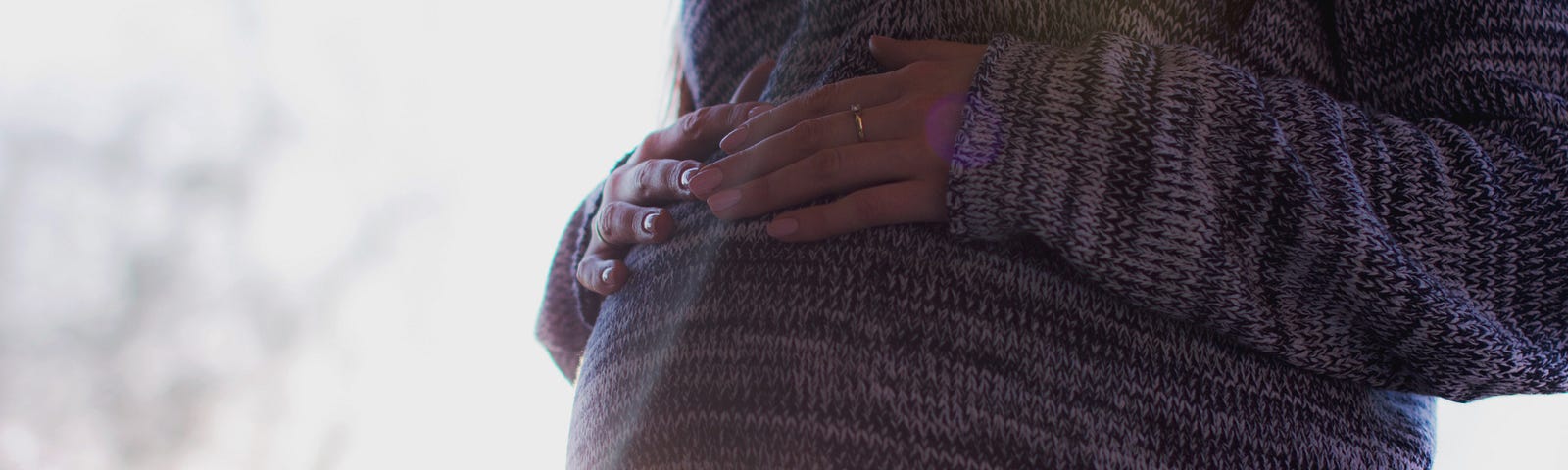 A pregnant person wearing a knitted sweater and holding their belly.