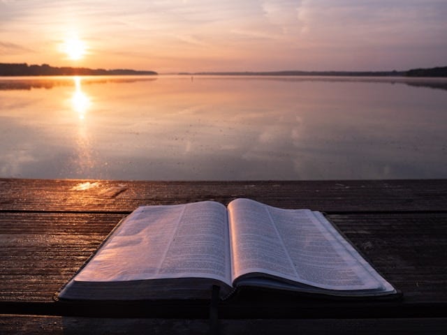 Bible on top of a table acing the open water at sunset
