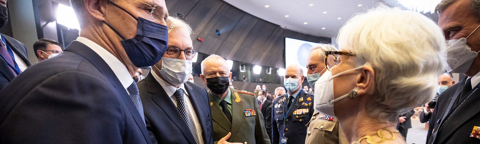 3 diplomats in masks shake hands.