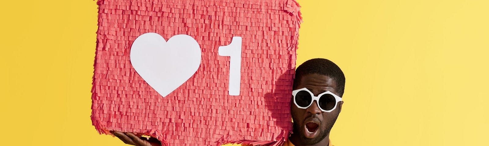 A black man wearing sunglasses on yellow background holding a like icon