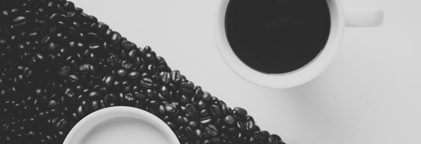 Image of table with coffee beans laid out on half, split diagonally. A mug on each side of the diagonal.