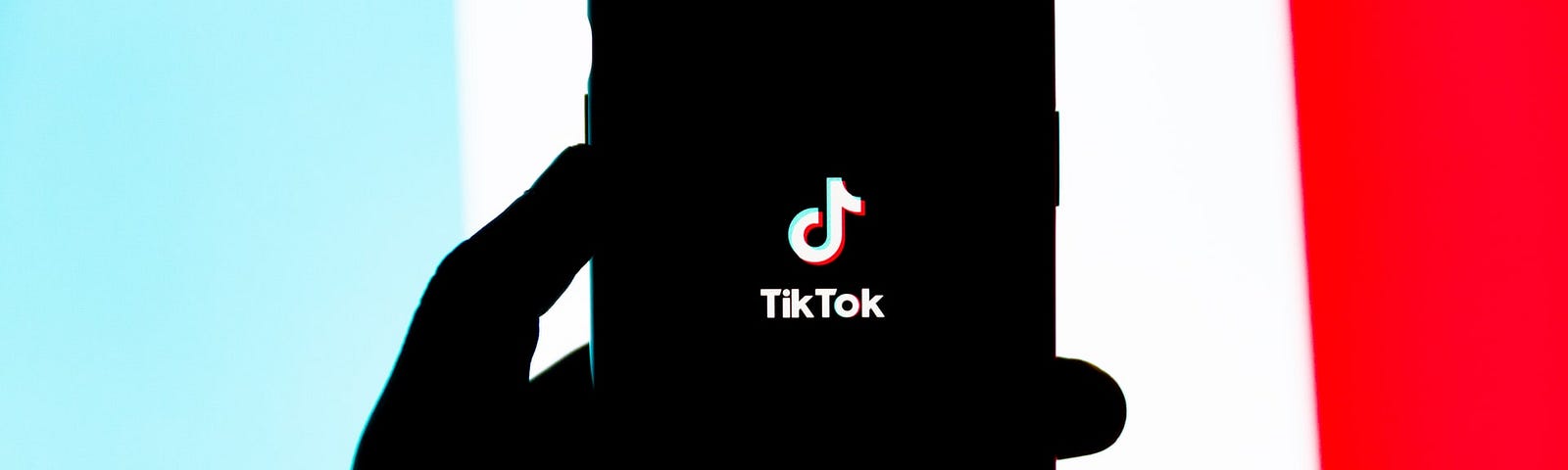 IMAGE: A hand holding a smartphone with the TikTok logo, all in black silhouette over the colors of the TikTok logo