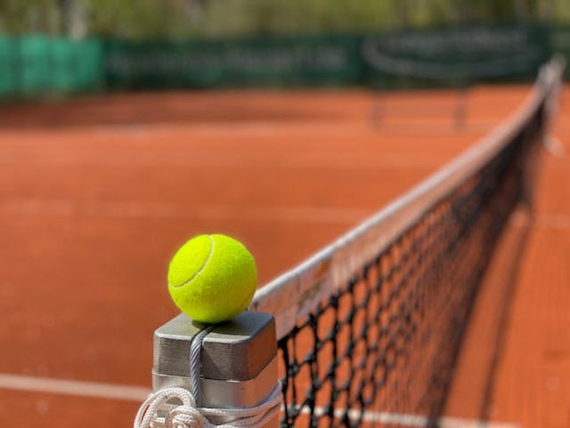 Tennis ball on tennis court balanced on post.