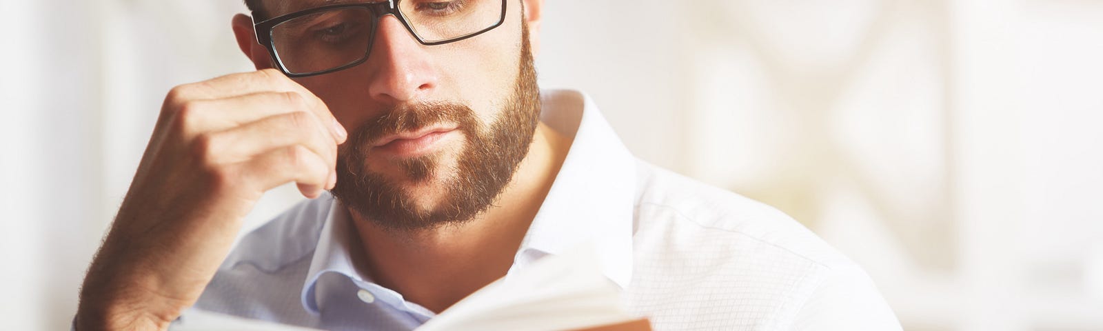 A man with a sad expression reading a red book.